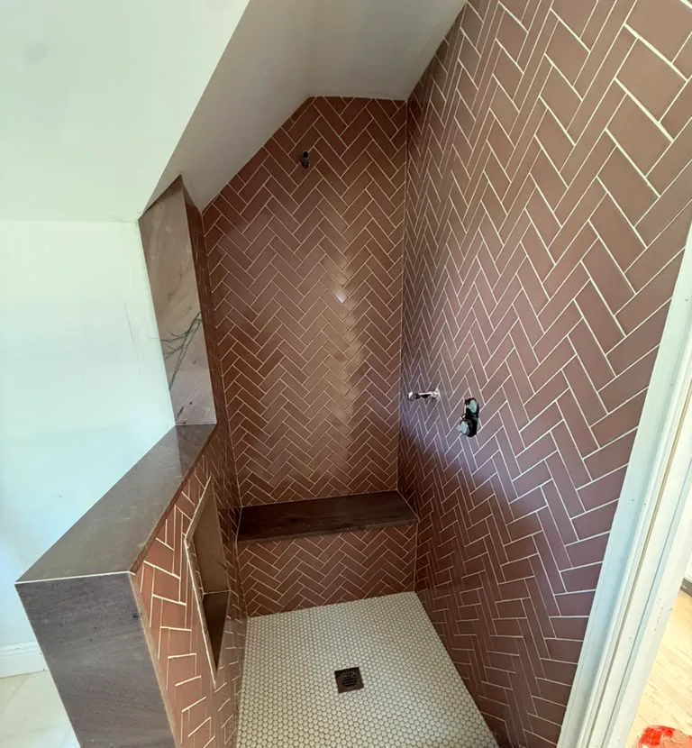 Finished shower with brown herringbone tile, stone bench and hexagon floor