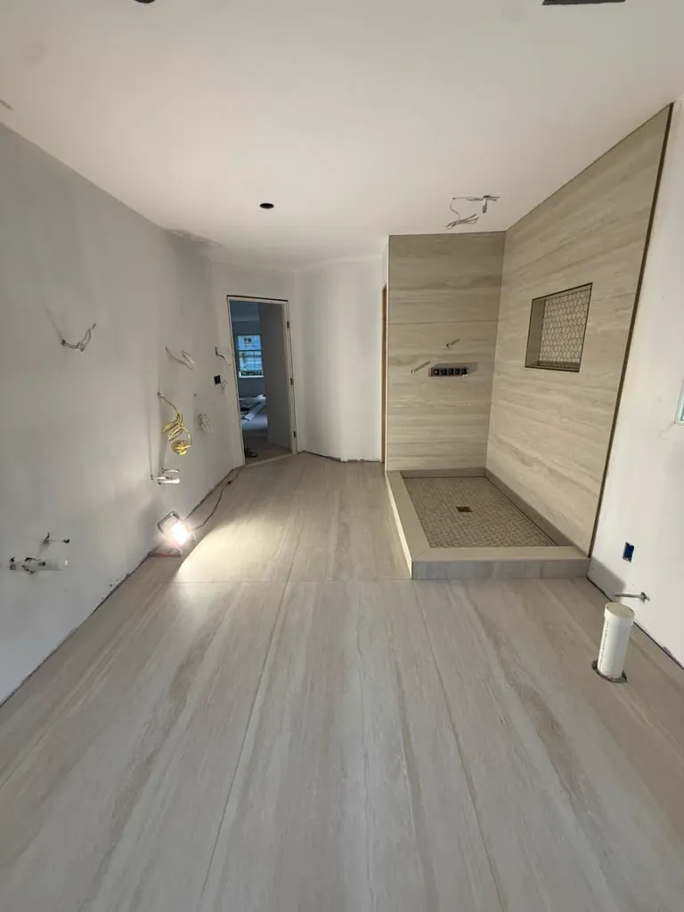 Long bathroom with travertine shower wall and wide plank flooring