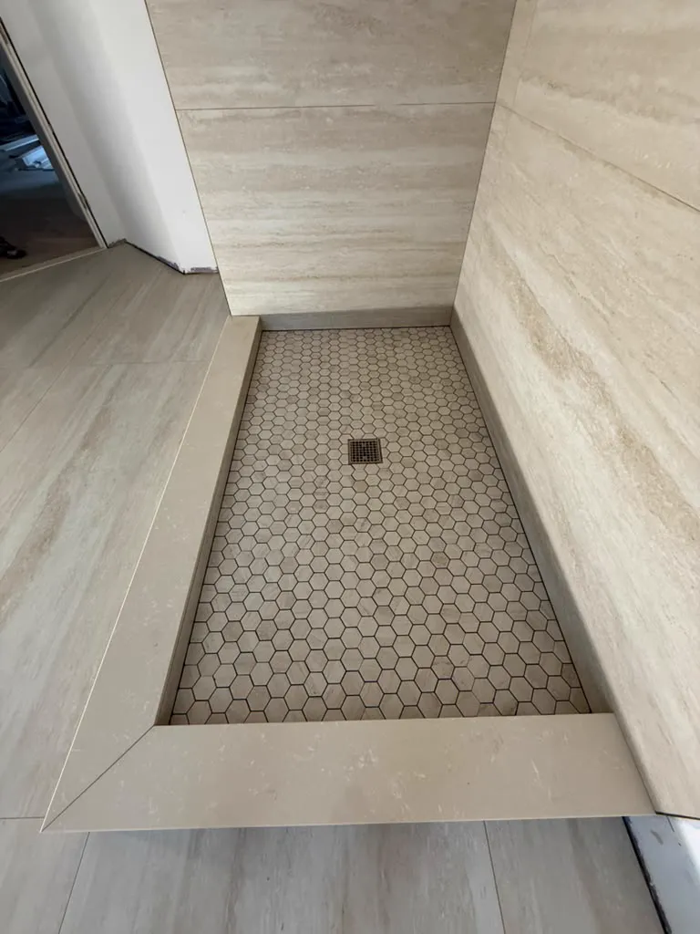 Travertine shower with hexagon mosaic floor and stone curb