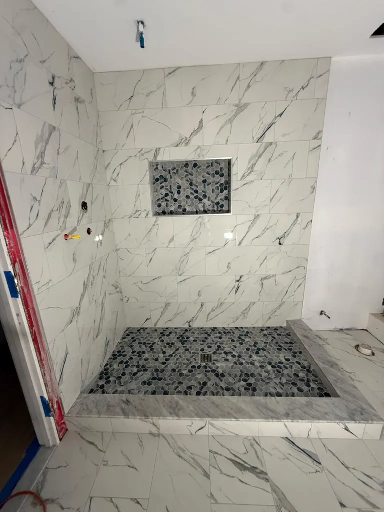 Marble tile shower with pebble floor and mosaic niche